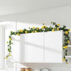 Yellow rose garland with green leaves draped over white kitchen cabinets in a bright, modern kitchen.
