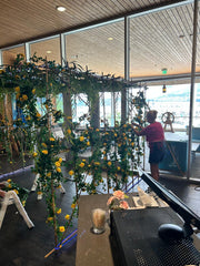A large floral arch made of weeping willow branches and yellow rose bush vines is being assembled for a Miami Vice Themed Night at KYC Yacht Club.