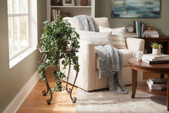 30" Artificial Pittsburgh Mini Leaf Trailing Ivy on a copper plant stand by a lounging chair.