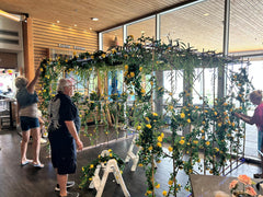 A large floral arch made of weeping willow branches and yellow rose bush vines is being assembled for a Miami Vice Themed Night at KYC Yacht Club.