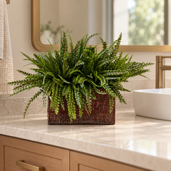 Artificial PVC button fern in a brown rectangular container with raised lettering on a modern bathroom vanity