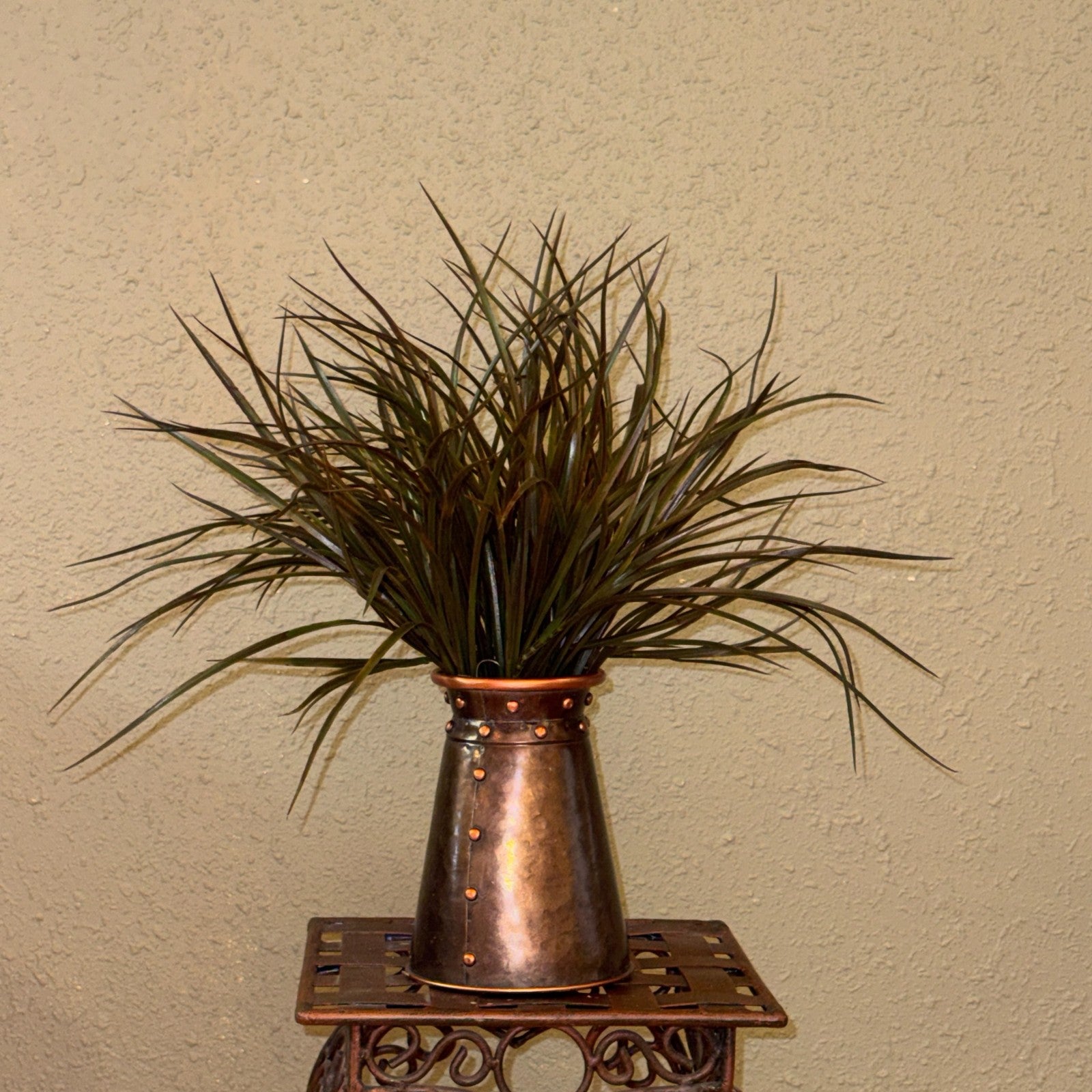 Original photograph of the 21-inch artificial sage green and brown grass arrangement in its riveted copper-tone container; display stand not included.