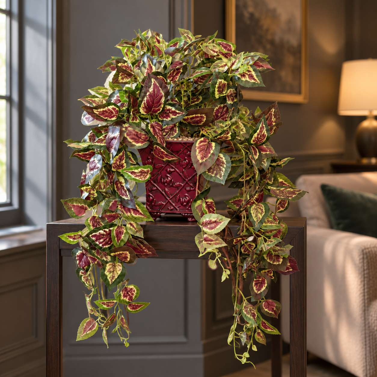 Trailing artificial silk coleus in a burgundy embossed metal planter, softly lit beside a living room window