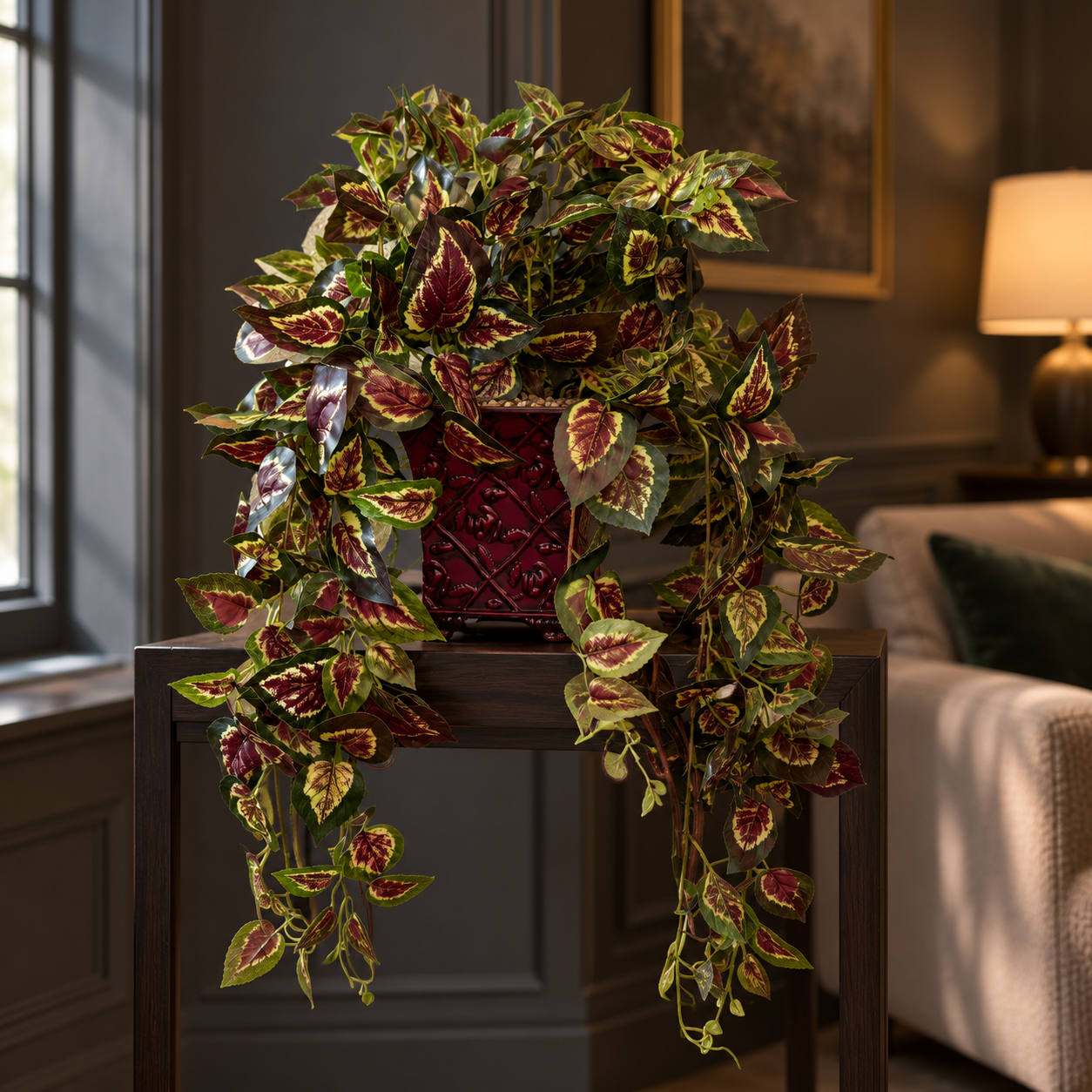 Trailing artificial silk coleus with burgundy, cream and green leaves in a burgundy metal planter in a moody living room