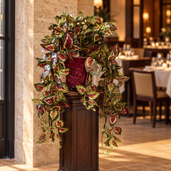 Trailing artificial silk coleus in a burgundy decorative metal planter on a wood pedestal in an upscale restaurant entryway